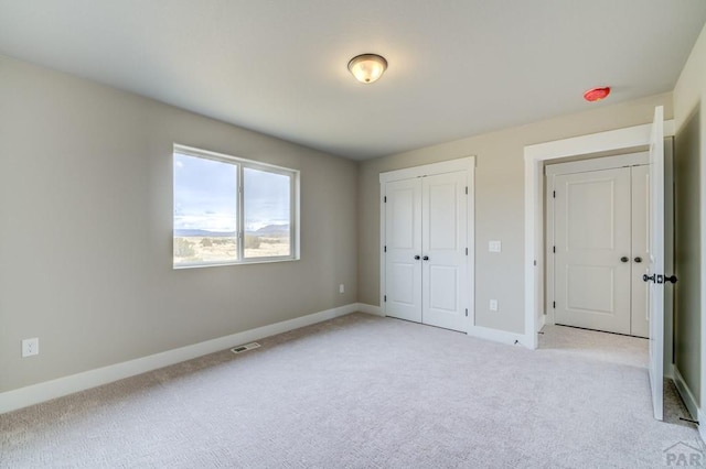 unfurnished bedroom featuring baseboards, a closet, visible vents, and light colored carpet