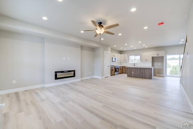 unfurnished living room featuring light wood-style flooring, recessed lighting, a ceiling fan, baseboards, and a glass covered fireplace