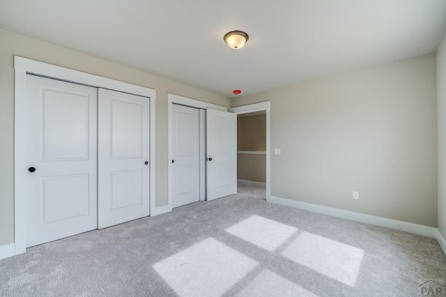 unfurnished bedroom featuring light carpet, baseboards, and two closets