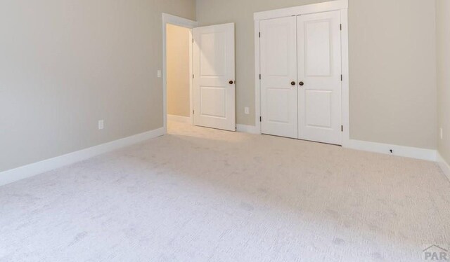 unfurnished bedroom with a closet, light colored carpet, and baseboards