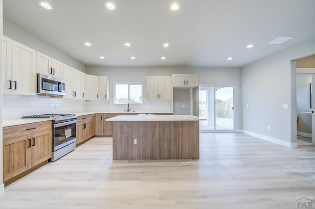 kitchen featuring appliances with stainless steel finishes, light countertops, a kitchen island, and a sink