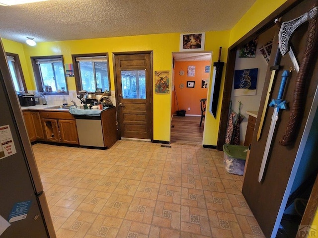 400 W Walnut St, Lamar, CO 81052 - kitchen with appliances with stainless steel finishes, a textured ceiling, brown cabinetry, baseboards, and a sink