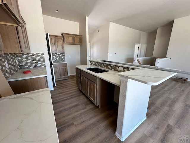 962 E Sandusky Dr, Pueblo West, CO 81007 - kitchen with dark wood-type flooring, decorative backsplash, a large island, brown cabinetry, and light stone counters