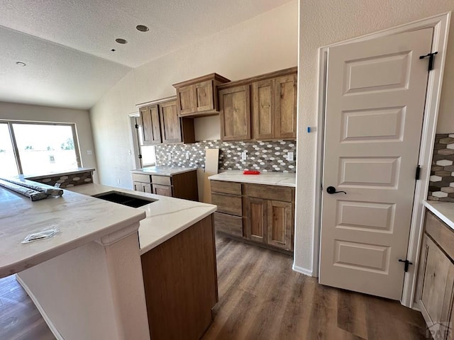 962 E Sandusky Dr, Pueblo West, CO 81007 - kitchen with vaulted ceiling, tasteful backsplash, dark wood finished floors, brown cabinetry, and a textured ceiling