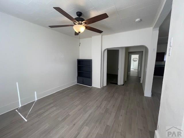 unfurnished living room with dark wood-style floors, ceiling fan, arched walkways, and baseboards