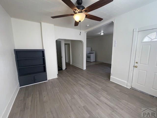 unfurnished living room featuring a ceiling fan, arched walkways, baseboards, and wood finished floors