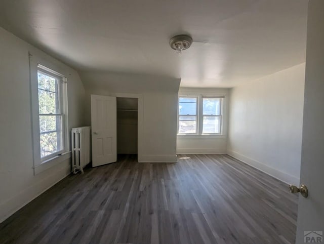 unfurnished bedroom featuring dark wood-style floors, multiple windows, radiator heating unit, and baseboards