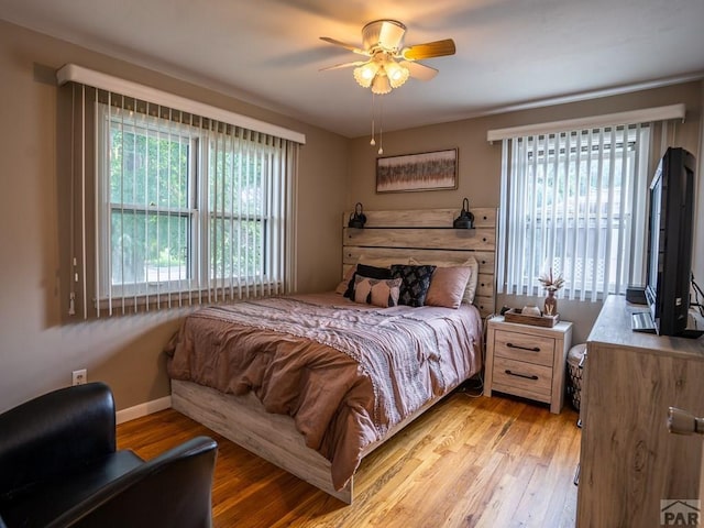 bedroom with light wood finished floors, baseboards, and a ceiling fan