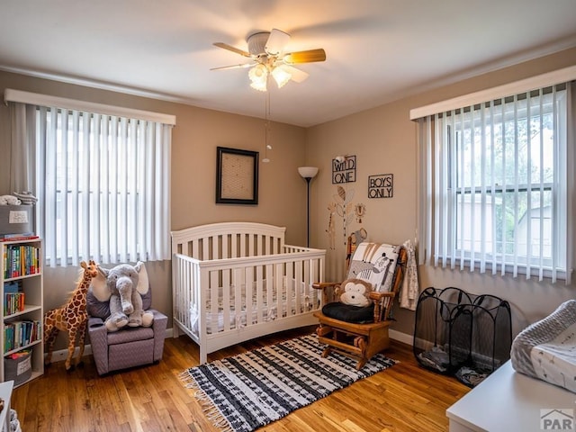 bedroom featuring a crib, light wood finished floors, ceiling fan, and baseboards