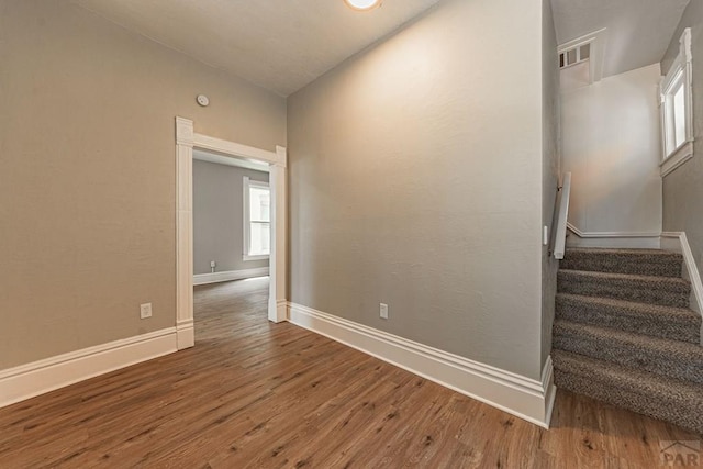 unfurnished room with stairway, wood finished floors, visible vents, and baseboards