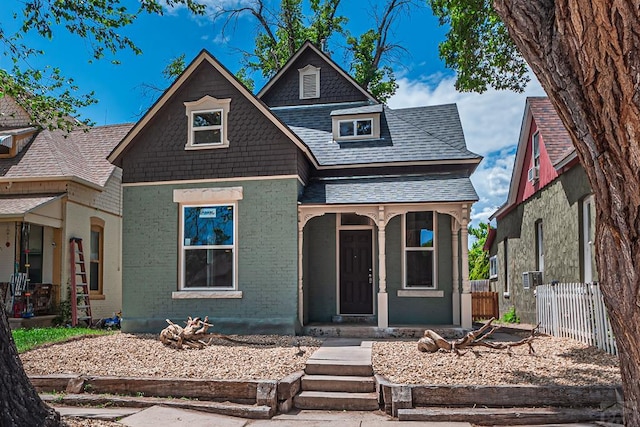 view of front of home with brick siding, a shingled roof, and fence