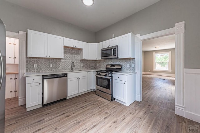 kitchen featuring light wood-style flooring, tasteful backsplash, white cabinetry, appliances with stainless steel finishes, and light countertops