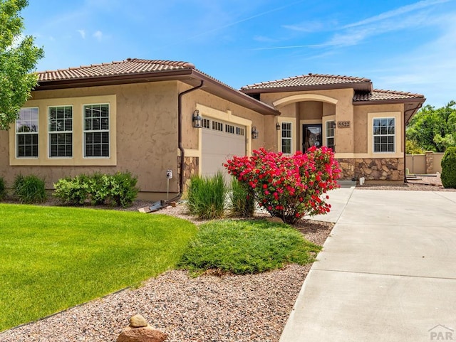 mediterranean / spanish-style house featuring a tile roof, stucco siding, an attached garage, a front yard, and stone siding