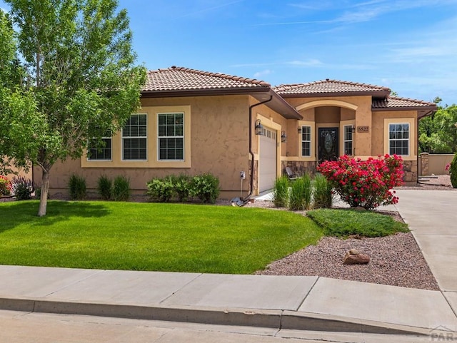 view of front of property with a garage, a tiled roof, a front yard, and stucco siding