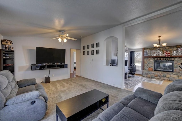 living room with arched walkways, a stone fireplace, light carpet, ceiling fan with notable chandelier, and baseboards