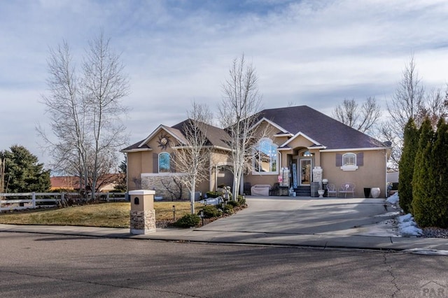 ranch-style house featuring driveway, fence, and stucco siding