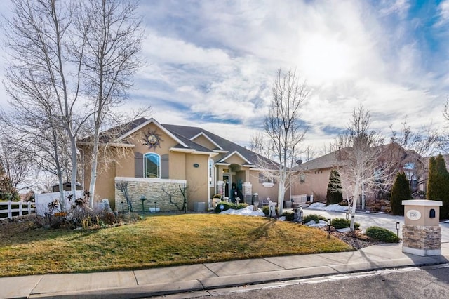 view of front of property with driveway, stone siding, a fenced front yard, a front lawn, and stucco siding