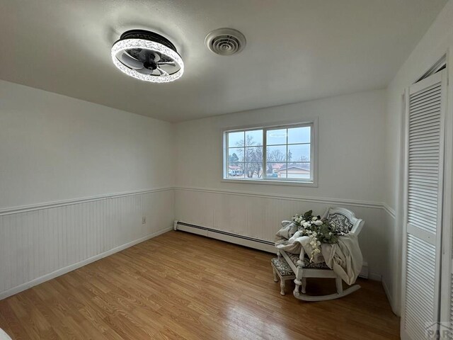 interior space with light wood-type flooring, a baseboard radiator, a wainscoted wall, and visible vents