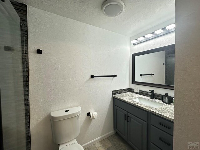 bathroom featuring a textured ceiling, a textured wall, toilet, vanity, and baseboards