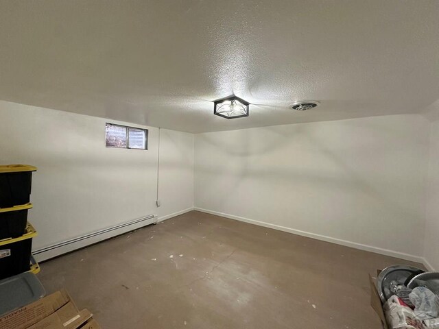 finished basement with a baseboard heating unit, visible vents, a textured ceiling, and baseboards