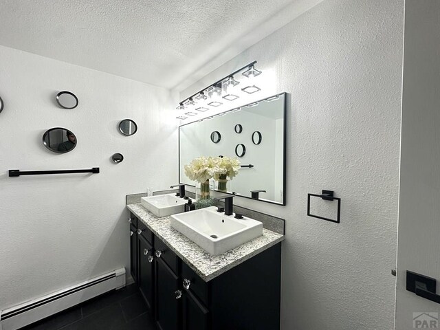 bathroom featuring a sink, a textured ceiling, baseboard heating, and double vanity