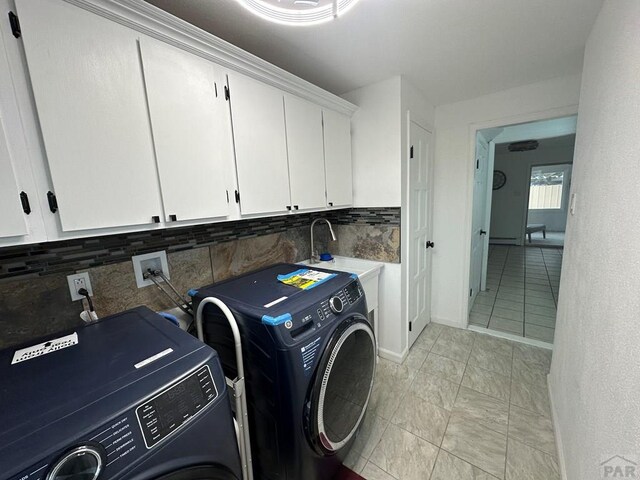 clothes washing area featuring separate washer and dryer, cabinet space, and baseboards