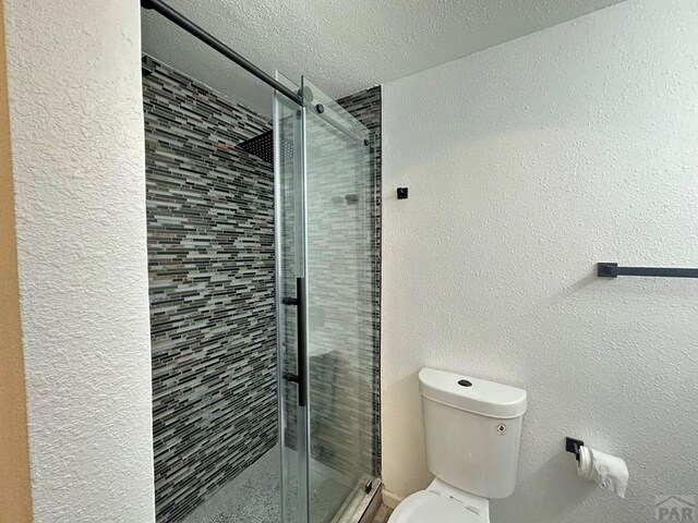 full bath featuring a textured wall, a shower stall, toilet, and a textured ceiling