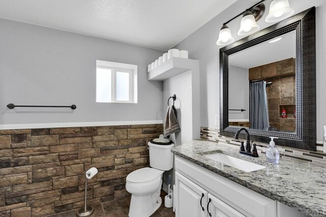 full bath featuring a wainscoted wall, tile walls, toilet, vanity, and a shower with curtain