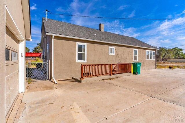 rear view of property with a shingled roof, a patio, a chimney, fence, and stucco siding