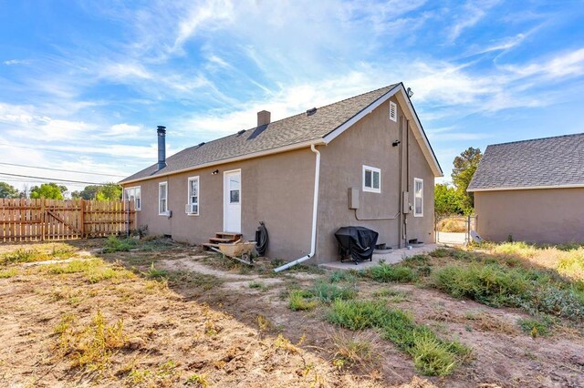 rear view of property with entry steps, a chimney, fence, and stucco siding