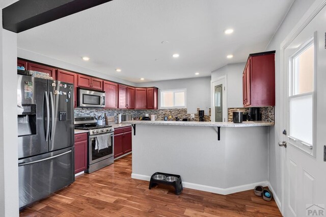 kitchen with tasteful backsplash, dark wood finished floors, appliances with stainless steel finishes, a peninsula, and dark brown cabinets