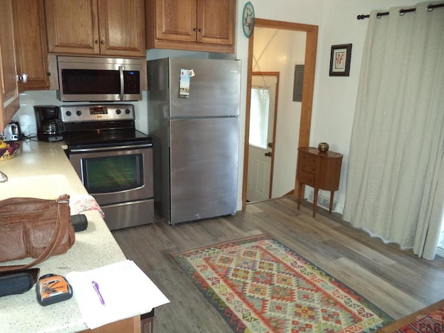 kitchen with dark wood-style floors, stainless steel appliances, light countertops, and brown cabinetry