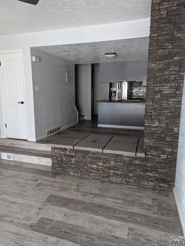 interior space with visible vents, a textured ceiling, baseboards, and wood finished floors