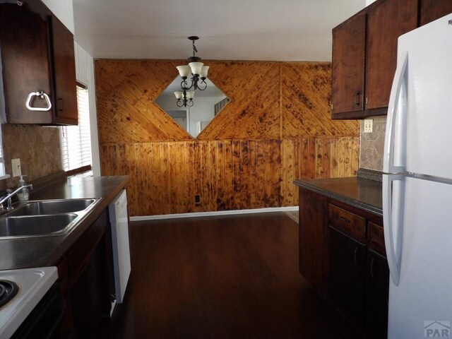 kitchen featuring a chandelier, white appliances, a sink, dark countertops, and decorative light fixtures