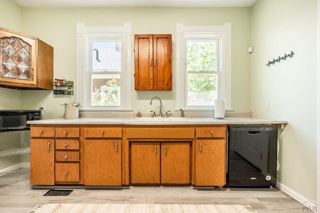 kitchen with brown cabinets, light wood finished floors, light countertops, dishwasher, and a sink