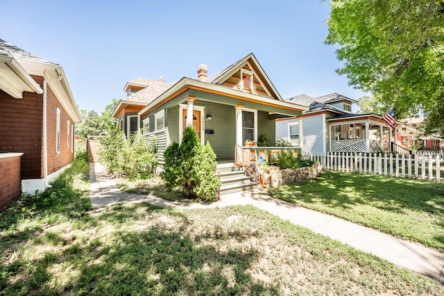 view of front of home featuring a porch, a front lawn, fence, and a chimney