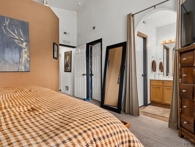 bedroom featuring arched walkways, ensuite bathroom, light carpet, a high ceiling, and visible vents