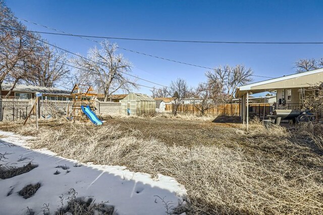 yard layered in snow with a playground, fence, an exterior structure, and an outdoor structure