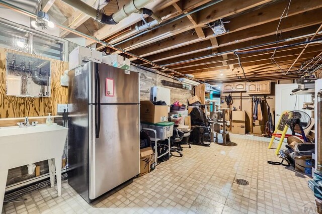 unfinished basement featuring light floors and freestanding refrigerator