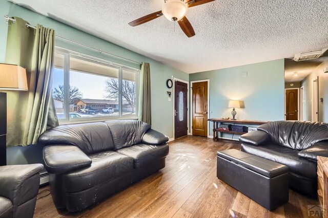 living room with a textured ceiling, visible vents, wood finished floors, and a ceiling fan