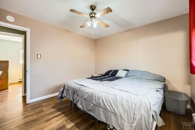 bedroom featuring baseboard heating, wood finished floors, a ceiling fan, and baseboards