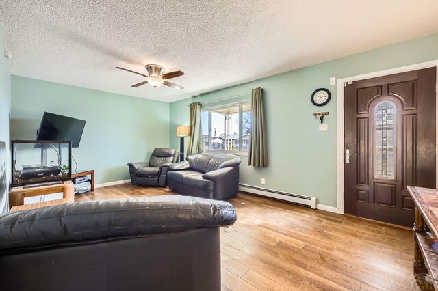 living area with baseboards, a ceiling fan, baseboard heating, a textured ceiling, and light wood-type flooring