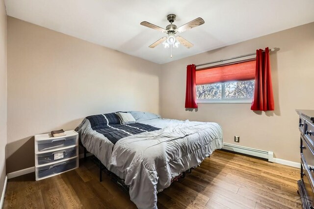 bedroom with a baseboard radiator, ceiling fan, baseboards, and wood finished floors