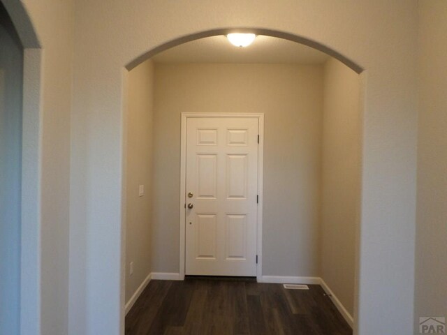 hallway with baseboards, arched walkways, and dark wood-type flooring