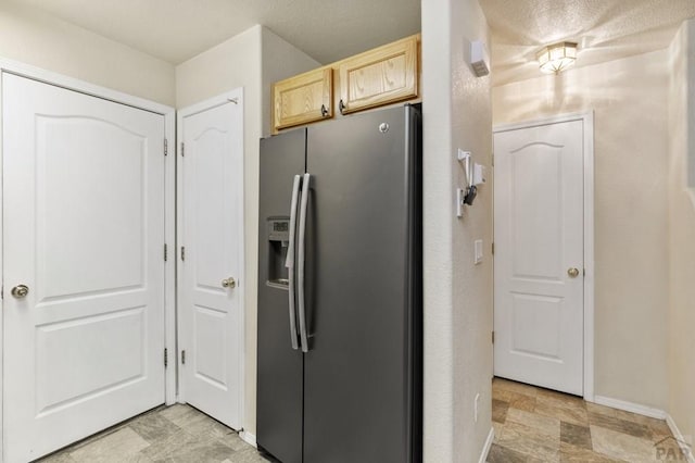 kitchen featuring stone finish flooring, light brown cabinets, stainless steel refrigerator with ice dispenser, and baseboards