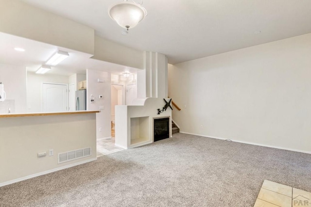 unfurnished living room with carpet floors, baseboards, a fireplace, and visible vents