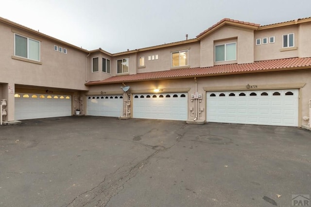 townhome / multi-family property featuring driveway, a tiled roof, an attached garage, and stucco siding