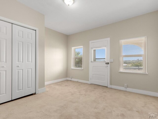 entryway featuring light carpet, a healthy amount of sunlight, and baseboards