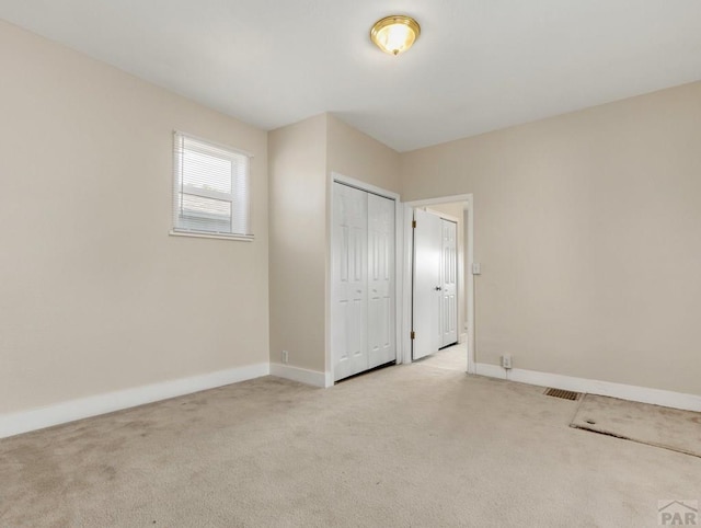 unfurnished bedroom with light carpet, a closet, and baseboards