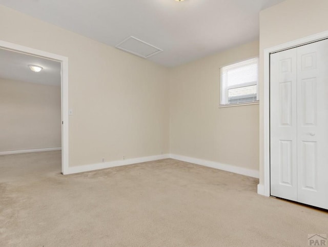 unfurnished bedroom featuring attic access, a closet, light carpet, and baseboards